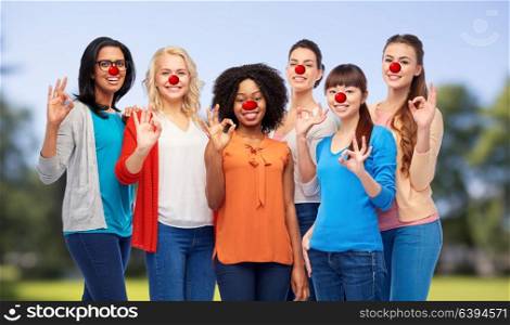 red nose day, diversity and people concept - international group of happy smiling different women with clown noses showing ok hand sign over natural background. group of women showing ok sign at red nose day