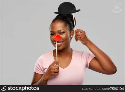 red nose day, party props and photo booth concept concept - happy african american young woman with clown nose over grey background. happy african american woman with red clown nose