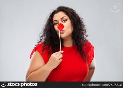 red nose day, party props and photo booth concept - happy woman with clown nose posing over grey background. happy woman with red clown nose posing