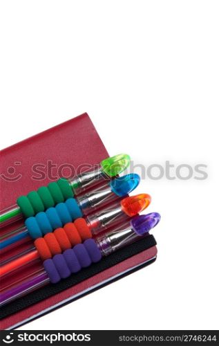 red notebook diary or agenda and colored pens lying on the top (isolated on white background)