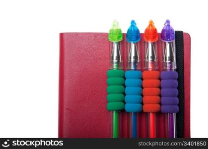 red notebook diary or agenda and colored pens lying on the top (isolated on white background)