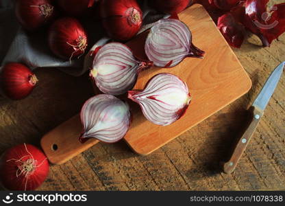 Red onions on wooden chopping cutting board on textile napkin over dark wooden rustic texture background. Top view, space for text .. Red onions on wooden chopping cutting board on textile napkin over dark wooden rustic texture background. Top view, space for text