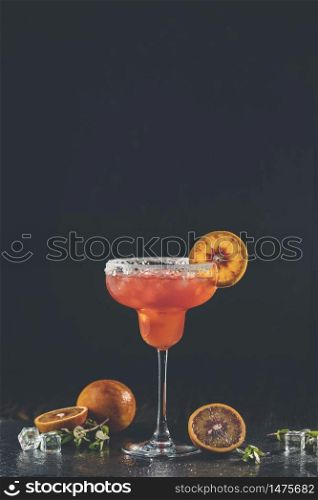 Red orange margarita cocktail with tequila, triple sec, orange juice, crushed ice and some salt on the rim of a glass, decorated with a citrus slice Shallow depth of the field Dark stone background