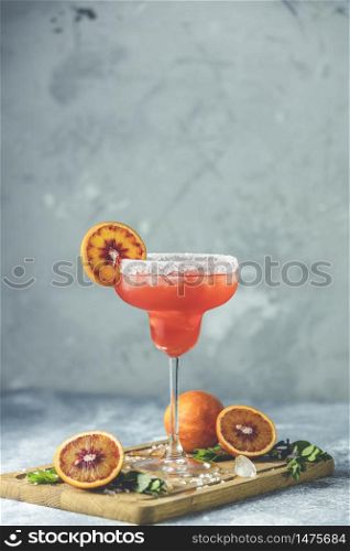 Red orange margarita cocktail with tequila, triple sec, orange juice, crushed ice and some salt on the rim of a glass, decorated with a citrus slice Shallow depth of the field, light stone background