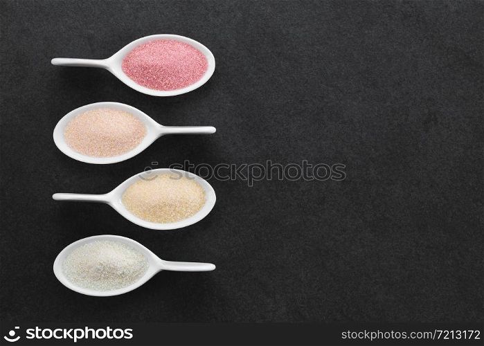 Red, orange, yellow and green instant jelly or jello powders on small spoons, photographed overhead on slate with copy space on the right side. Jelly or Jello Powders
