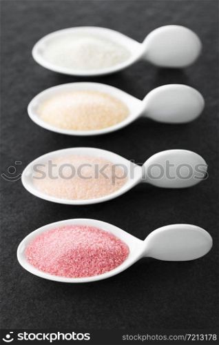 Red, orange, yellow and green instant jelly or jello powders on small spoons, photographed on slate (Selective Focus, Focus in the middle of the red powder). Jelly or Jello Powders