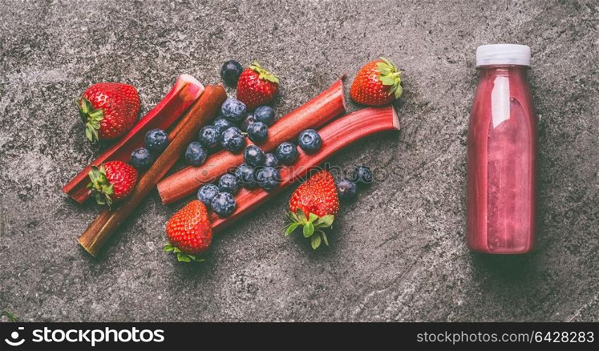Red organic fruits and berries smoothie with rhubarb, blueberries and strawberries in bottle on gray granite table , top view. Healthy dieting and antioxidant beverage