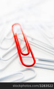 Red paper clip on top of clusters of white ones.