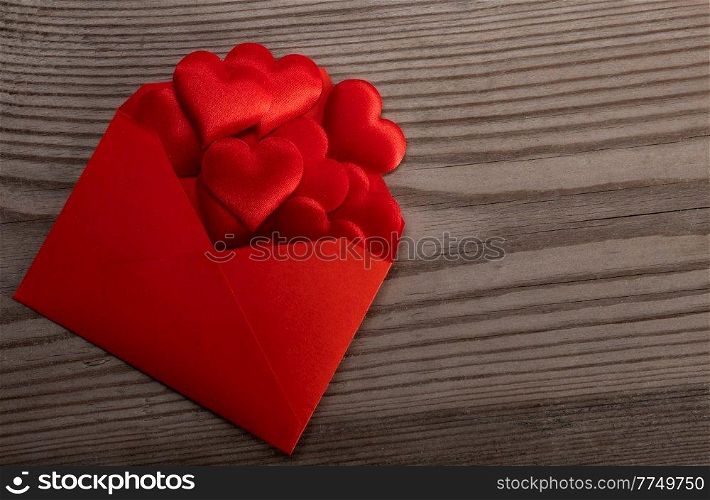 Red paper envelope with Valentines hearts on wooden background. Flat lay, top view. Romantic love letter for Valentine’s day concept.. Red envelope with red hearts