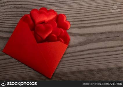 Red paper envelope with Valentines hearts on wooden background. Flat lay, top view. Romantic love letter for Valentine&rsquo;s day concept.. Red envelope with red hearts