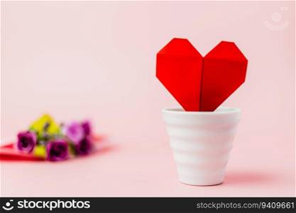 Red paper heart in white flower pot with blurred purple rose bouquet on pink background for love and Valentine&rsquo;s day concept