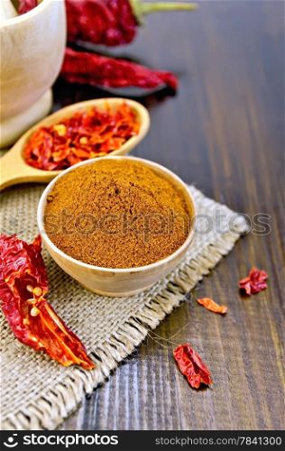 Red pepper powder in a wooden bowl, cereal and dry chili pepper pods in a wooden spoon and a mortar, sacking on a wooden board