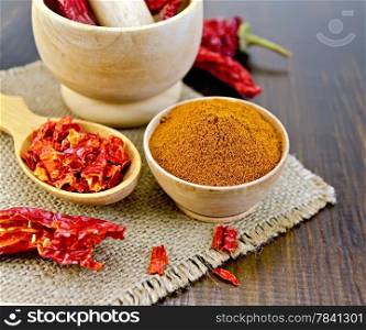 Red pepper powder in a wooden bowl of dry cereal and pods of red pepper in a mortar and a wooden spoon, sacking on a wooden board