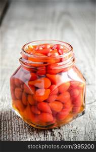 Red peppers drops in glass jar on the wooden background