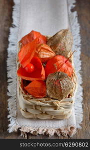 red Physalis fruits in straw basket, isolated on old wooden background