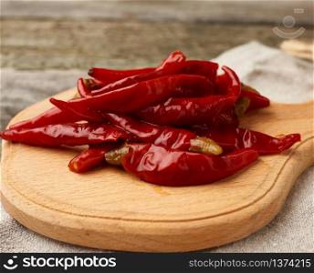 red pickled mini chili peppers on a wooden board, hot spice for meat