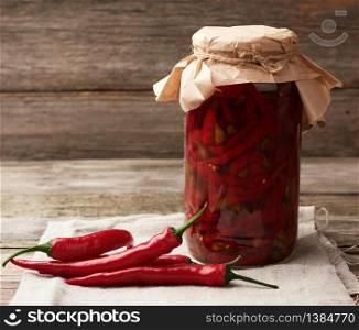 red pickled mini chilli peppers in a glass jar and fresh fruits nearby, spicy meat spice