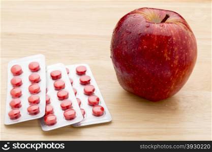 Red pills blister pack and red apple. Red pills blister pack and red apple on wooden background