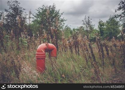 Red pipeline on a rural meadow with plants and trees