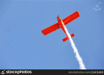 Red plane emits smoke in the blue sky. Air show. Red plane emits smoke in blue sky