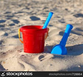 red plastic bucket and blue rake, shovel on the sand, summer background