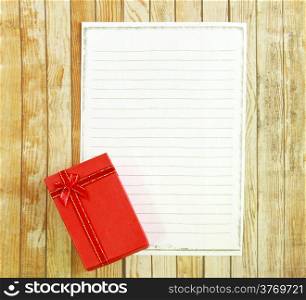 Red present box with blank note paper on wooden background