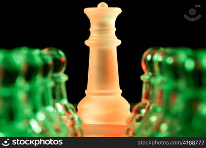 red queen and rows of green glass chess pawns is standing on board in dark