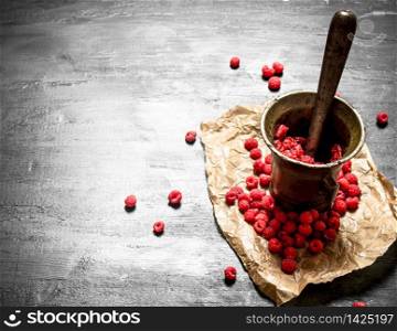 Red raspberries in a mortar with pestle. On a black wooden background.. Red raspberries in a mortar with pestle.