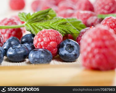 red raspberry lies with the blueberry berries on the table, summertime, photo of ripe and tasty berries close up. raspberry with blueberry