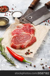 Red raw beef rib eye steak fillet with steel hatchets on light table background with salt and pepper.