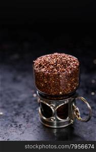 Red raw quinoa in a glass cup, dark background, selective focus