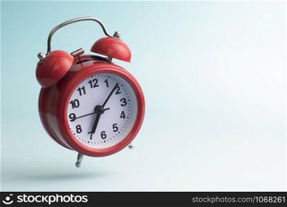 Red retro style alarm clock flying on blue background.