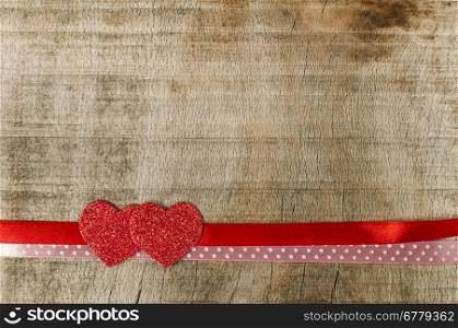 Red ribbon tape and hearts on wooden background.