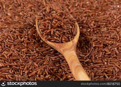 Red rice in a wooden spoon on red rice background