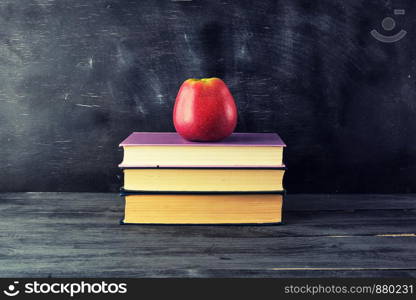 red ripe apple lies on a stack of books, black background, back to school