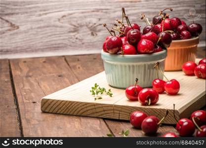 Red ripe cherries in ceramic bowls on wooden kitchen countertop.