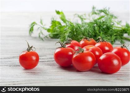 Red ripe cherry tomatoes and green dill on a wooden table