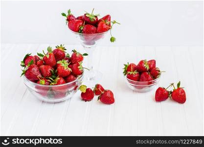 Red ripe strawberries in a glass bowl on a white wooden table. Harvest from your garden. The concept of healthy eating.. Red ripe strawberries in a glass bowl on a white wooden table. Harvest from your garden.