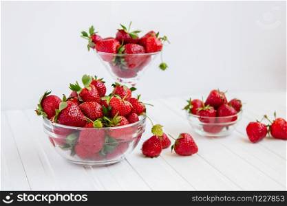 Red ripe strawberries in a glass bowl on a white wooden table. Harvest from your garden. The concept of healthy eating.. Red ripe strawberries in a glass bowl on a white wooden table. Harvest from your garden.