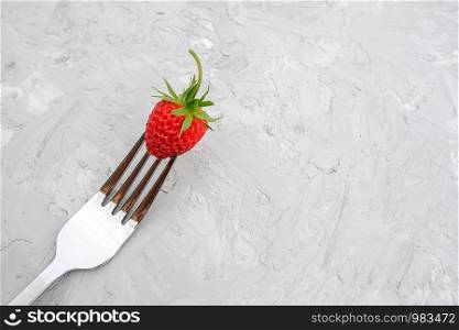 Red ripe strawberry on fork on background of gray stone table with copy space. Concept diet food or vegetarianism. Minimal style Top view.. Red ripe strawberry on fork on background of gray stone table with copy space. Concept diet food or vegetarianism. Minimal style Top view