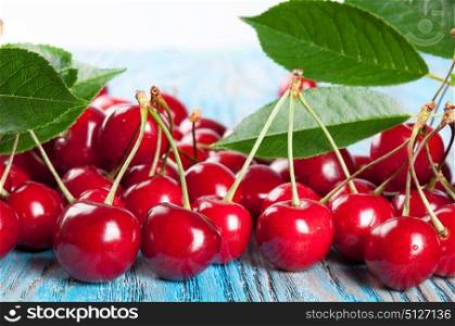 Red ripe sweet cherry and green leaves on a blue wooden background