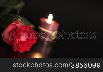 Red rose and candle on black background.