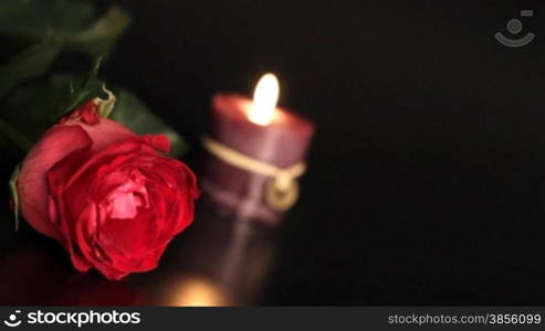 Red rose and candle on black background.