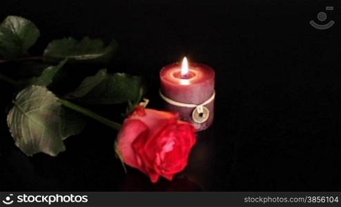 Red rose and candle on black background.