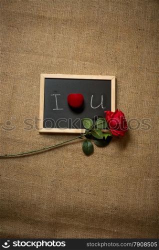 Red rose and wedding ring lying on declaration of love written on chalkboard