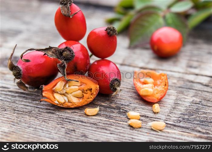 Red rosehips and cut berries in half with seeds on a wooden table. Close-up.. Red rosehips and cut berries in half with seeds on a wooden table.