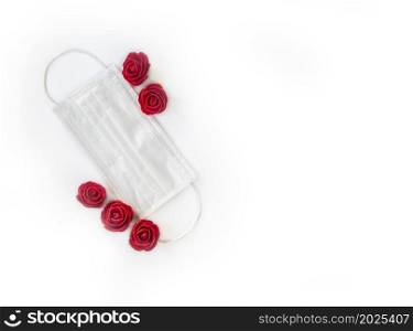 Red roses and a protective medical face mask isolated on white background. Safe Valentine&rsquo;s Day during the coronavirus pandemic. Covid-19 and Valentine concept space for text. Red roses and a protective medical face mask isolated on white background. Safe Valentine&rsquo;s Day during the coronavirus pandemic. Covid-19 and Valentine concept