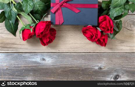 red roses surrounding dark gift box on weathered wooden background in flat lay view