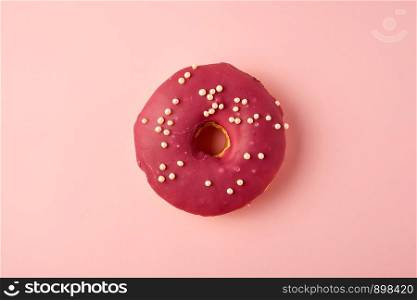 red round donut with white sprinkles on a pink background, top view