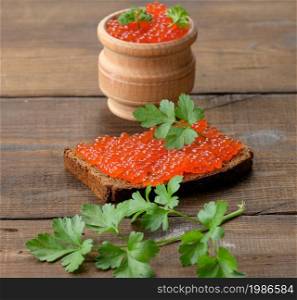 red salmon caviar lies on a piece of rye bread. Brown wooden table